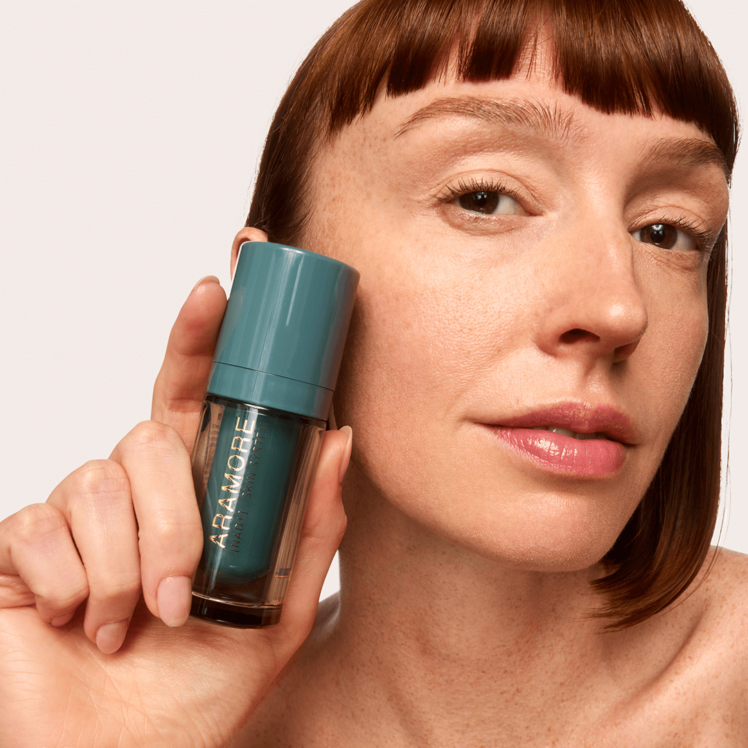 Person with red hair holding Aramore NAD+ Renewing Eye Cream Bottle on a white background