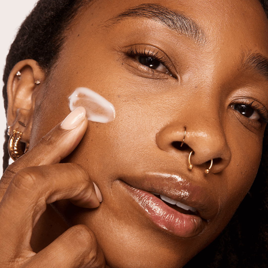 Woman applying NAD+ Cell Energizing Treatment serum to her face with a close-up focus on her skin texture.