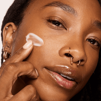 Woman applying NAD+ Cell Energizing Treatment serum to her face with a close-up focus on her skin texture.