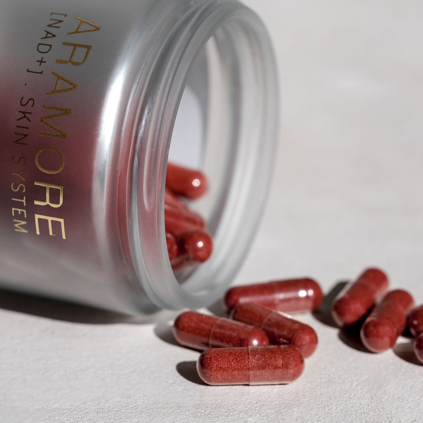 A jar of red capsules labeled 'ARAMORE NAD+ Skin System' spilled on a surface.