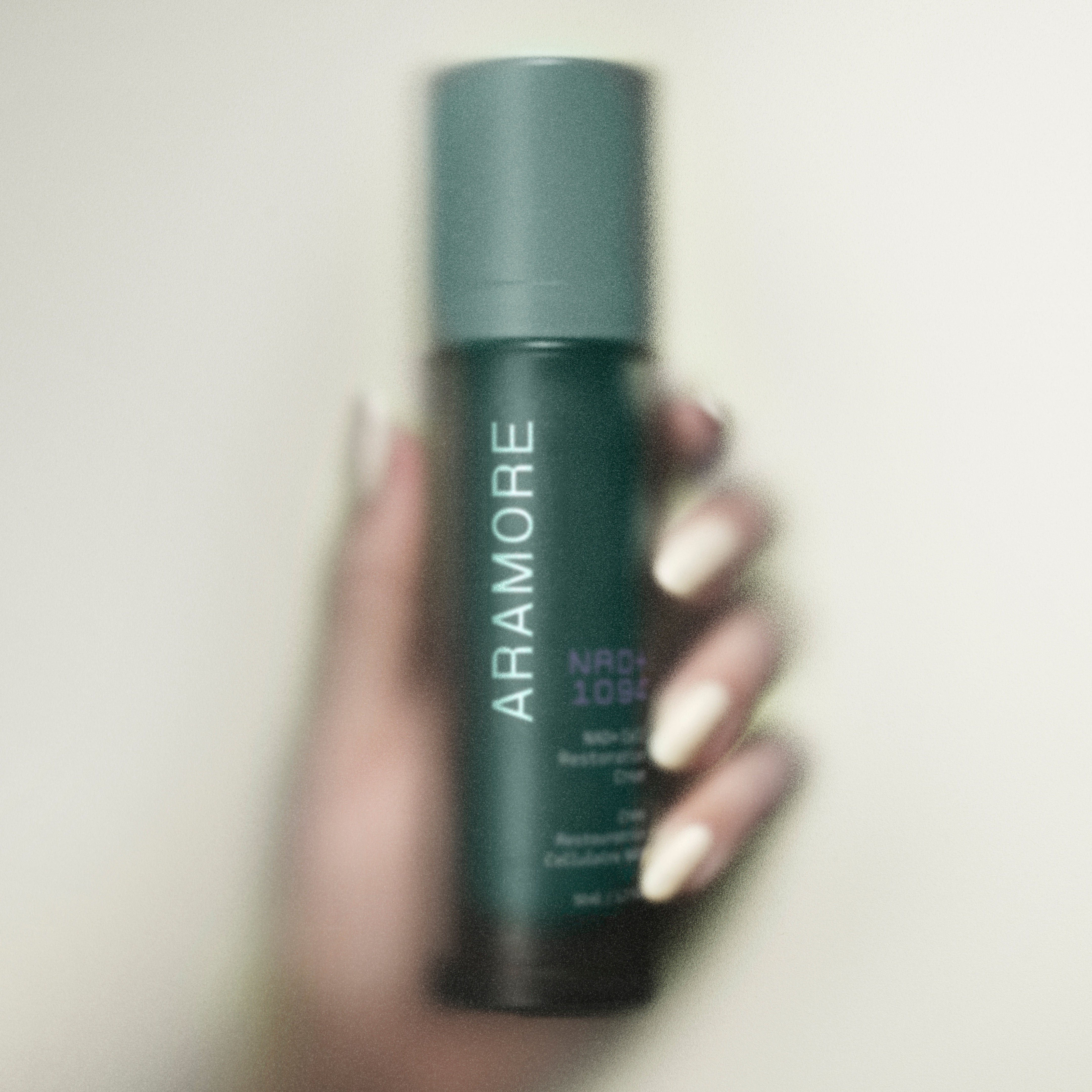 NAD+ Cell Restoration Cream being held by a woman's hand behind a mirrored glass surface