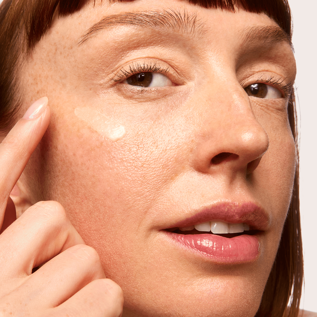 Person with red hair using NAD+ Renewing Eye Cream on a white background